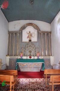 Foto da Igreja vista de dentro, mostrando alguns bancos e o altar