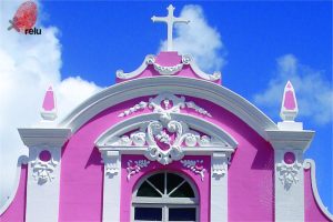 Foto da Capela do Bom Conselho focando na sua parte superior, mostrando parte de uma janela e a cruz em cima da capela.